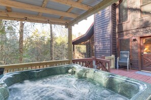 A hot tub under a wooden deck with a view of a rustic building and trees. - Waterfront Cabin w/ Beautiful River View & Hot Tub (Ellijay)
