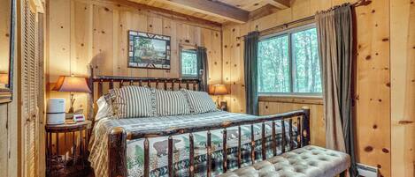 A wooden cabin bedroom with a bed, bedside lamps, a bench, and a window with curtains.