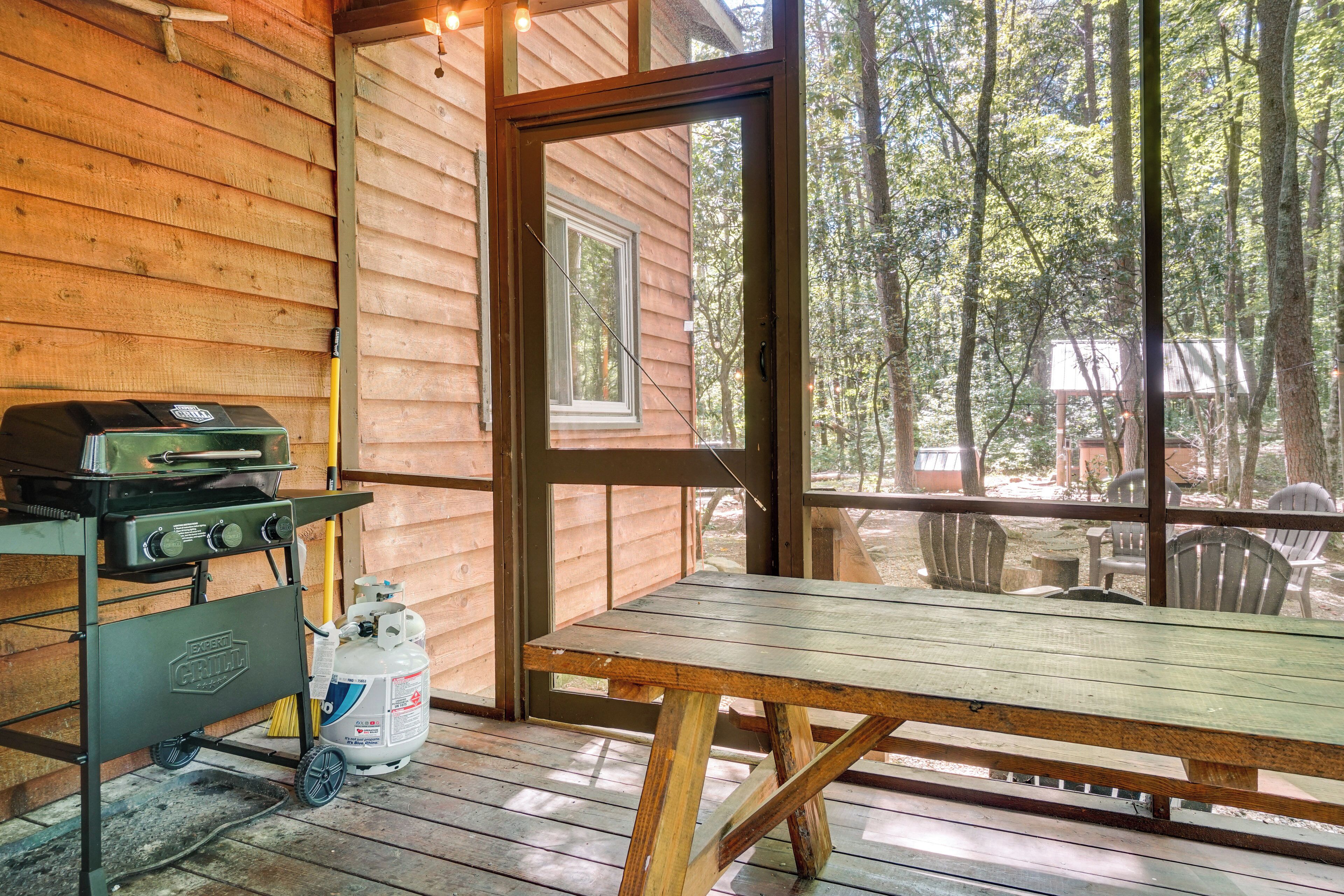 A wooden cabin with a large window, a grill, and a gas tank on the deck.