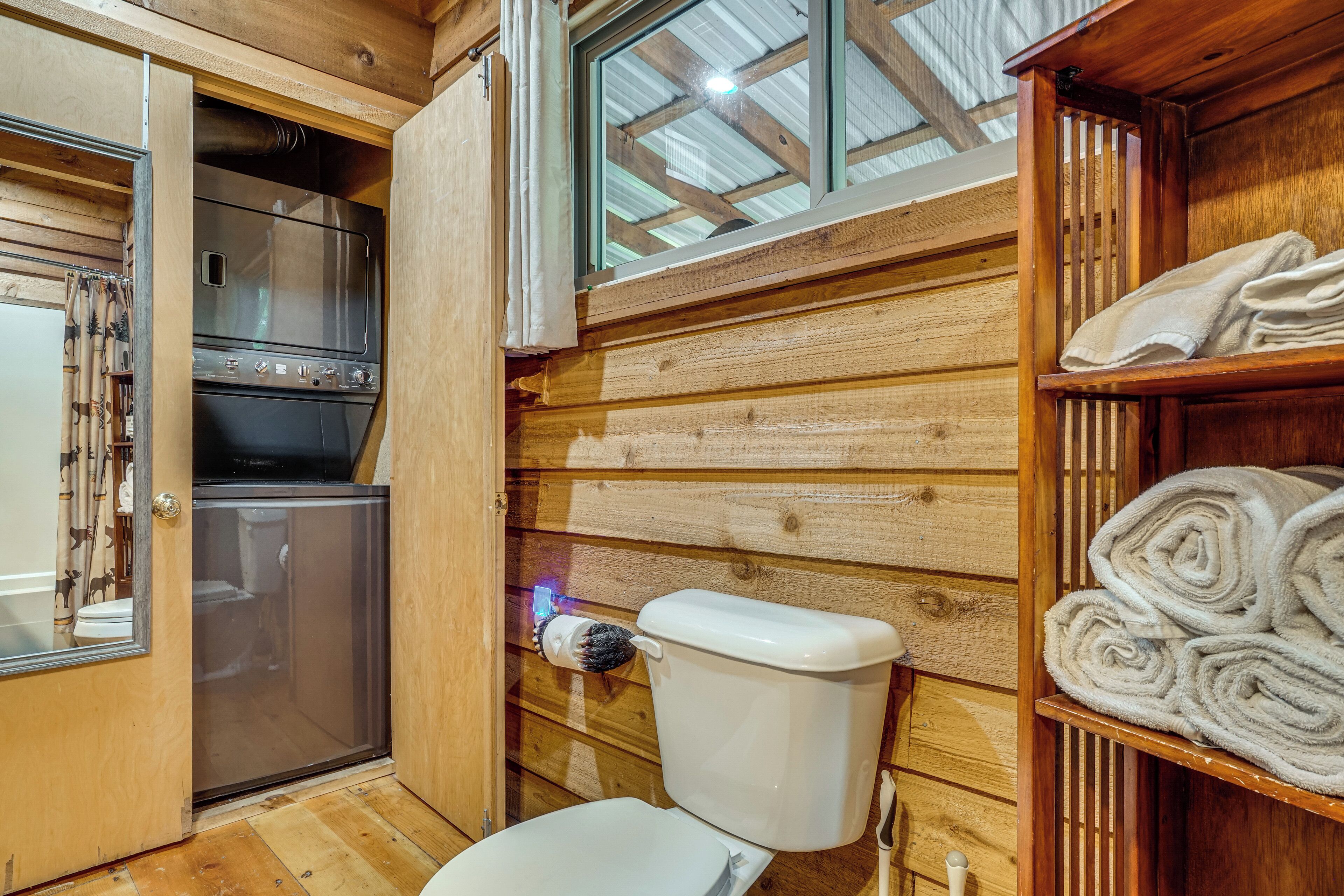 Eine gemütliche Holz-Blockhütte mit Küchenzeile, inklusive Kühlschrank und Herd, Toilette und Ablage mit gefalteten Handtüchern.
