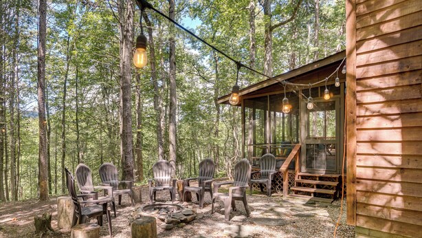 A rustic cabin with a fire pit and outdoor seating area surrounded by trees.