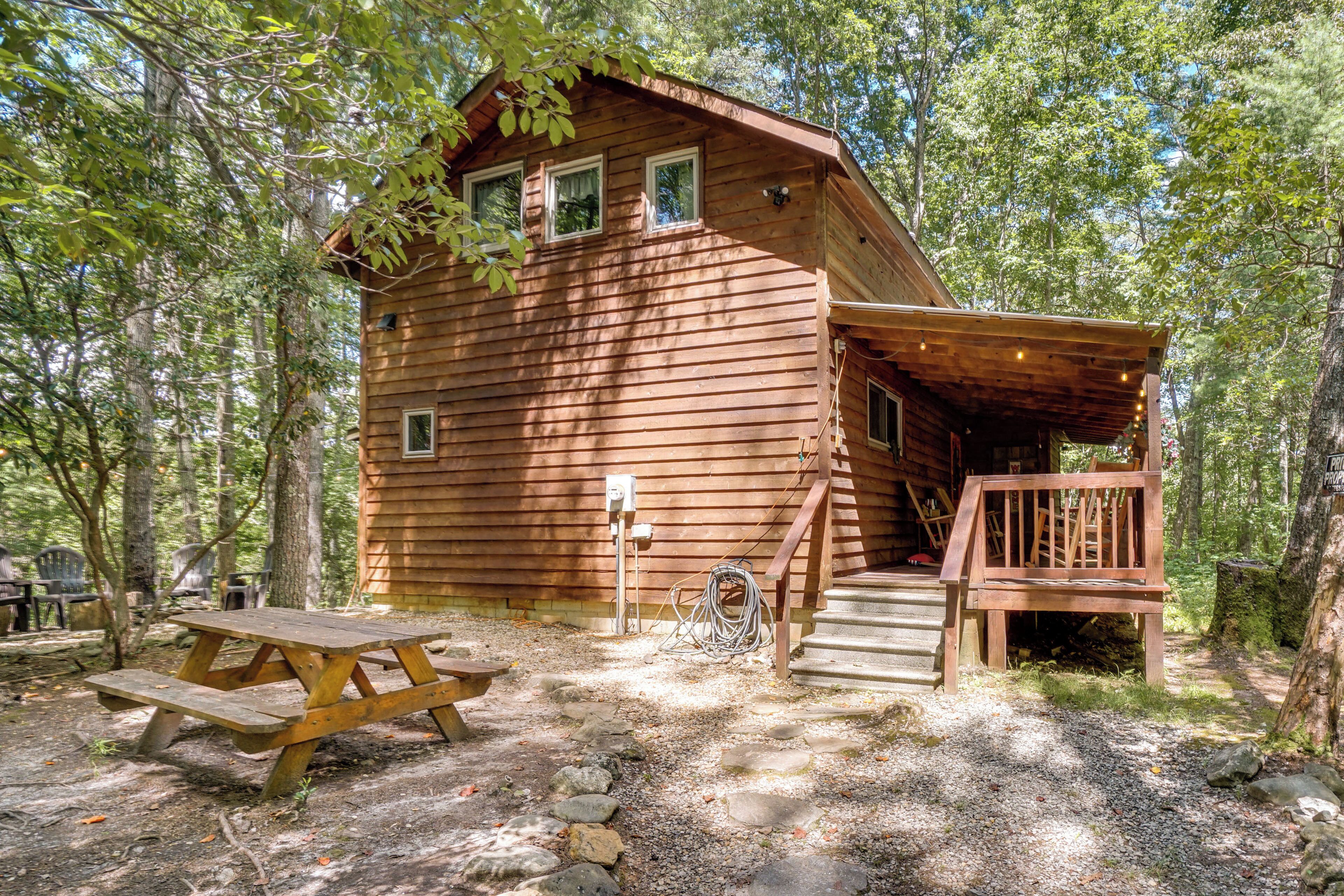 A wooden cabin with a porch and a picnic table in a forest setting.