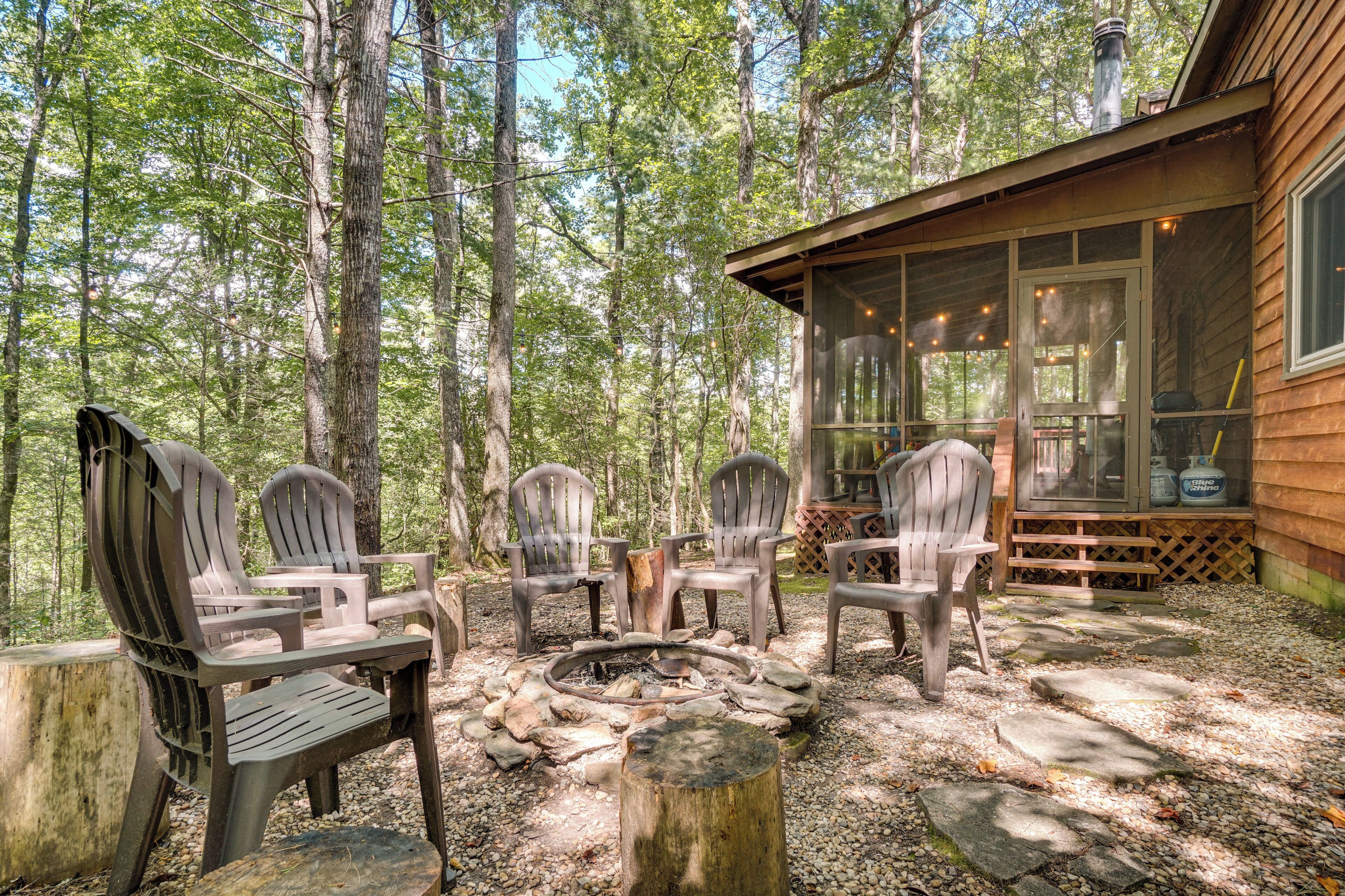 Eine Holzhütte mit Lagerfeuerstelle und Adirondack-Stühlen in Waldlandschaft.