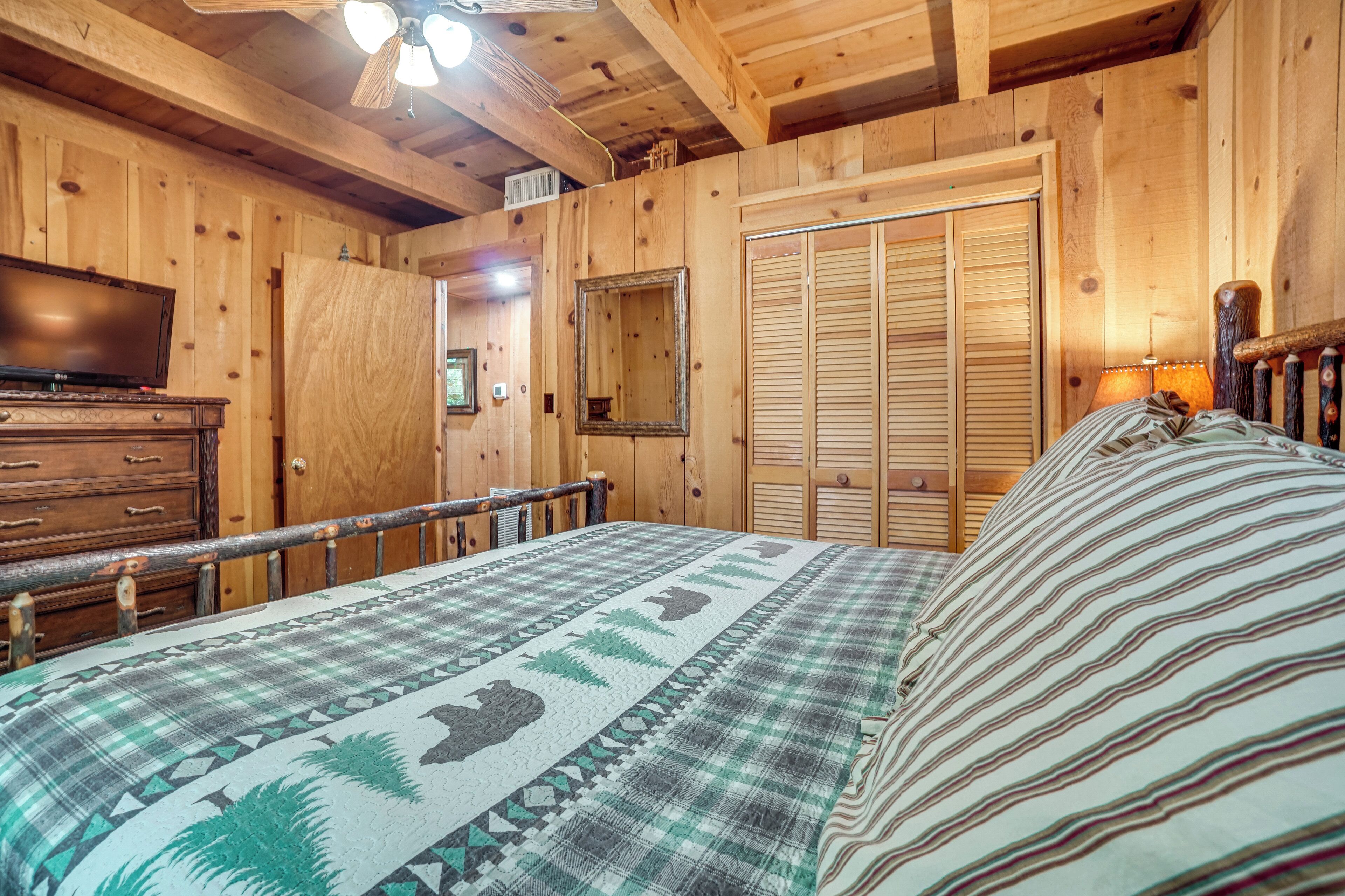 A wooden cabin bedroom with a bed, dresser, and a television.