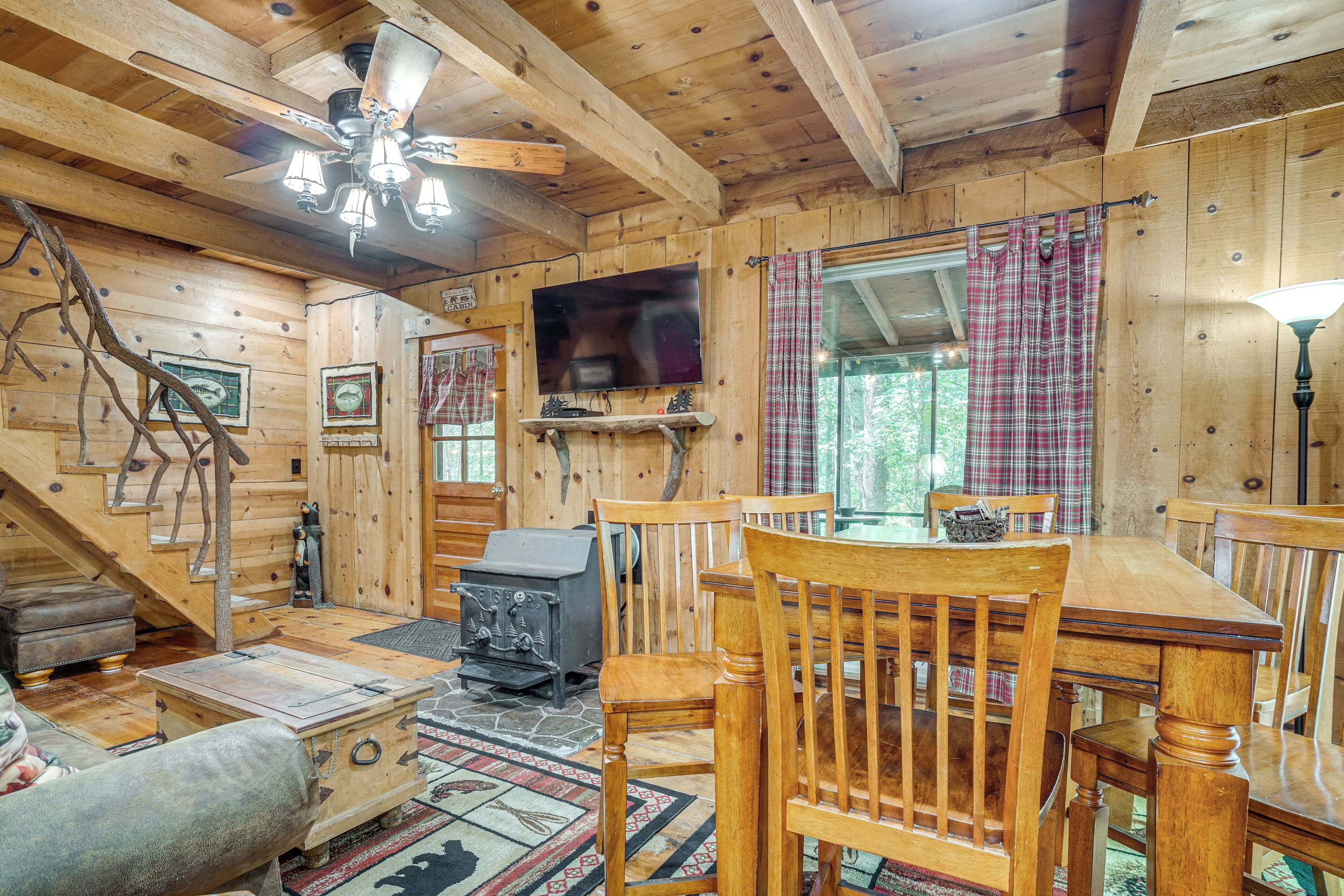 A wooden cabin interior with a dining table, chairs, a fireplace, a television, and a staircase.