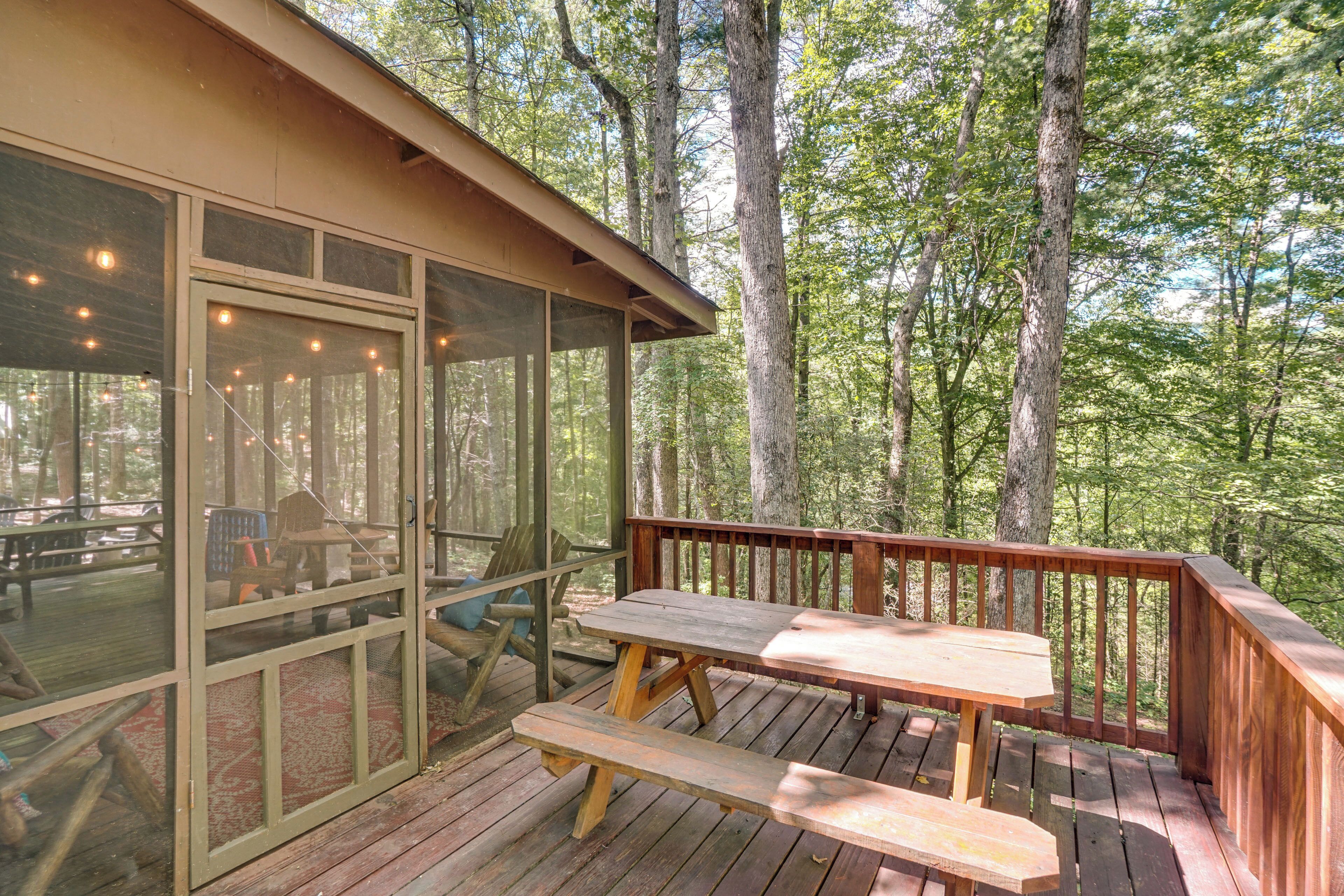 A wooden deck with picnic tables and a covered seating area, surrounded by trees.