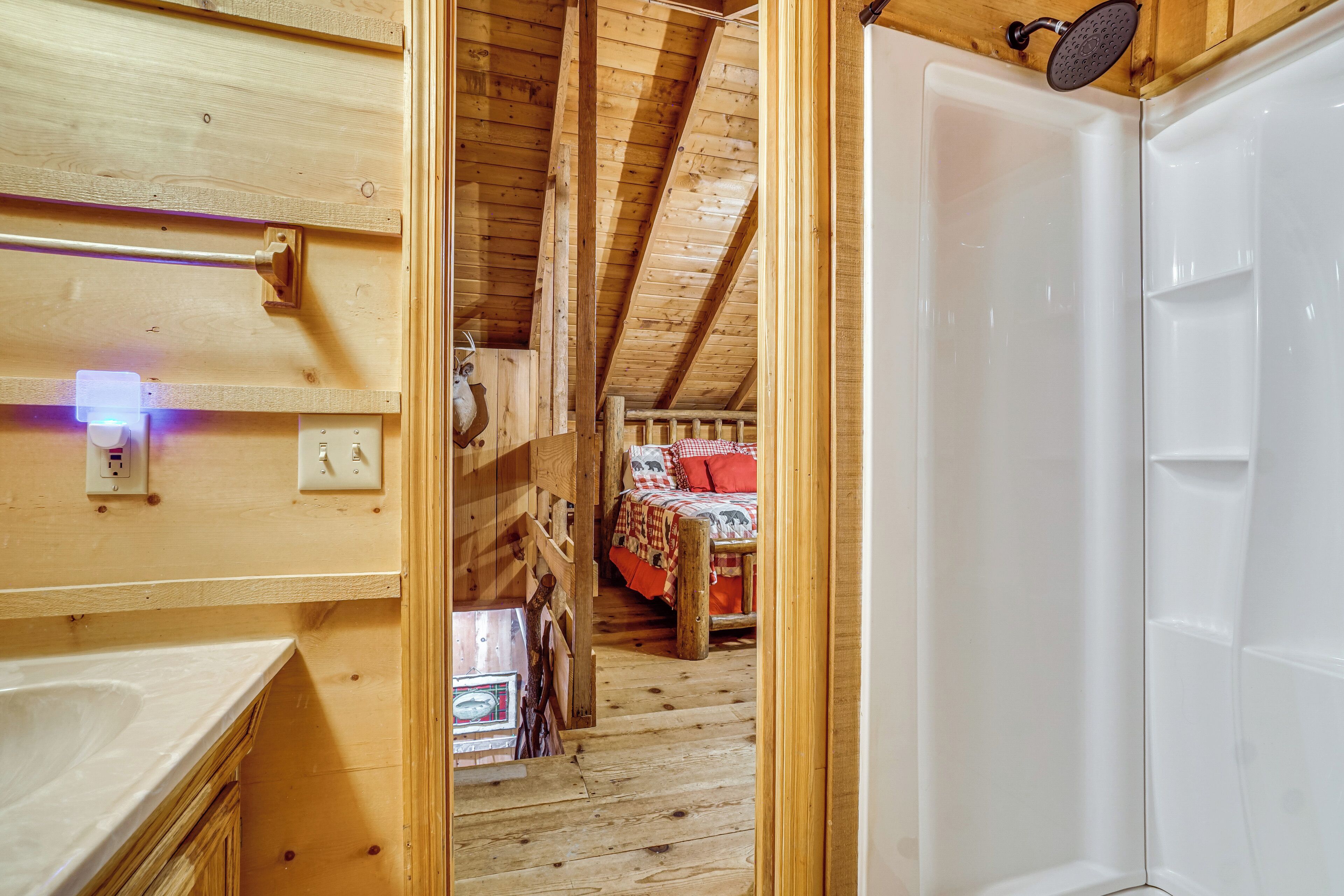 Ein Holzinnenraum mit einer weißen Badewanne, einem Bett mit roten Kissen und einer Holzbalkendecke.