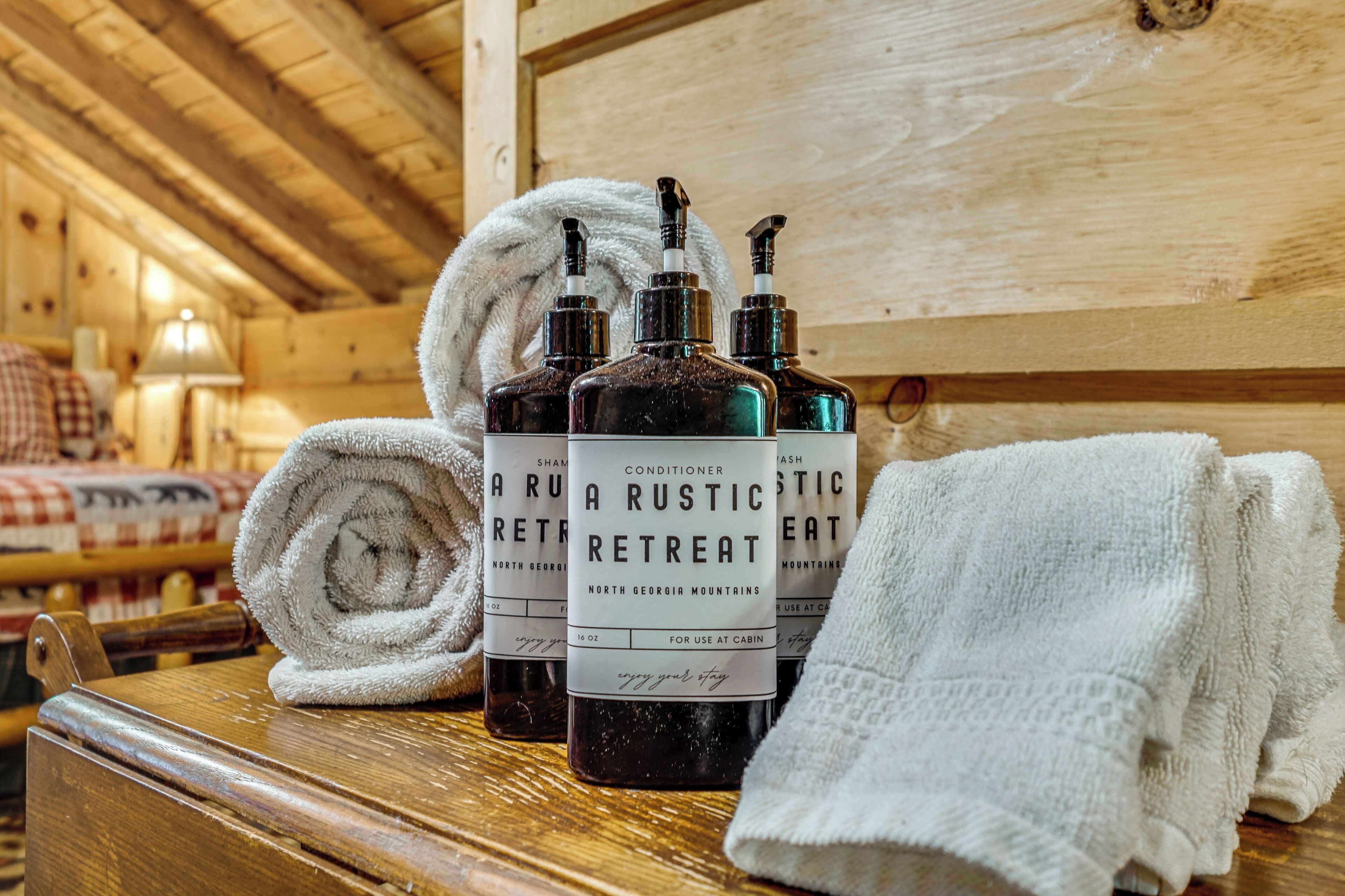 A wooden cabin interior with a wooden chest, three bottles of conditioner, and rolled towels.