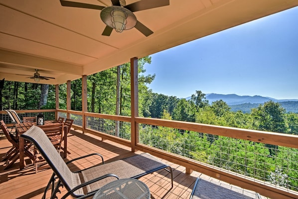 Eine überdachte Terrasse im Freien mit Holzmöbeln und Blick auf eine bewaldete Bergkette.