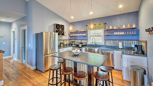 Una cocina moderna con una isla central, taburetes de bar, electrodomésticos de acero inoxidable y estanterías abiertas con frascos.