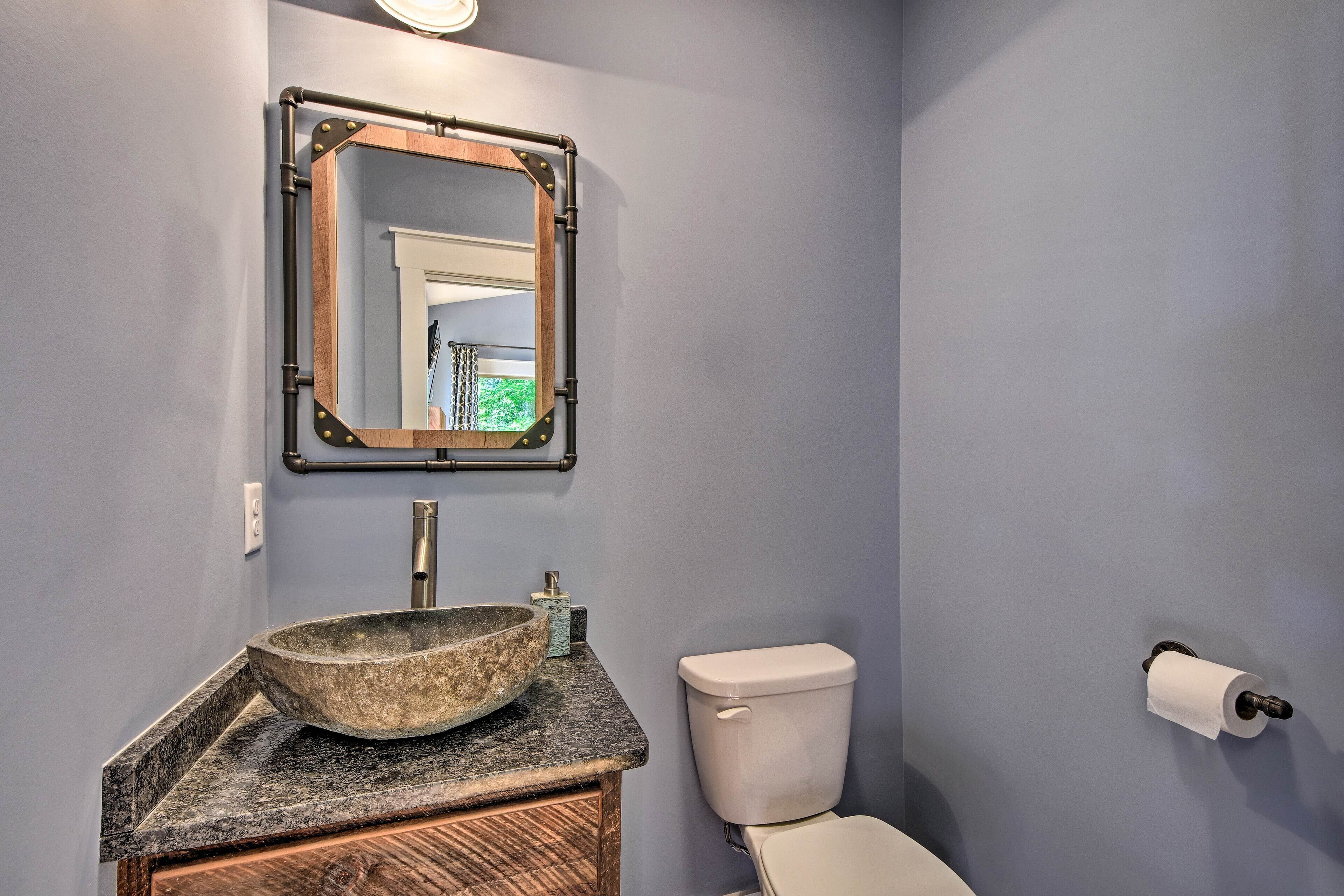 A bathroom with a stone sink, a toilet, and a mirror with a metal frame.