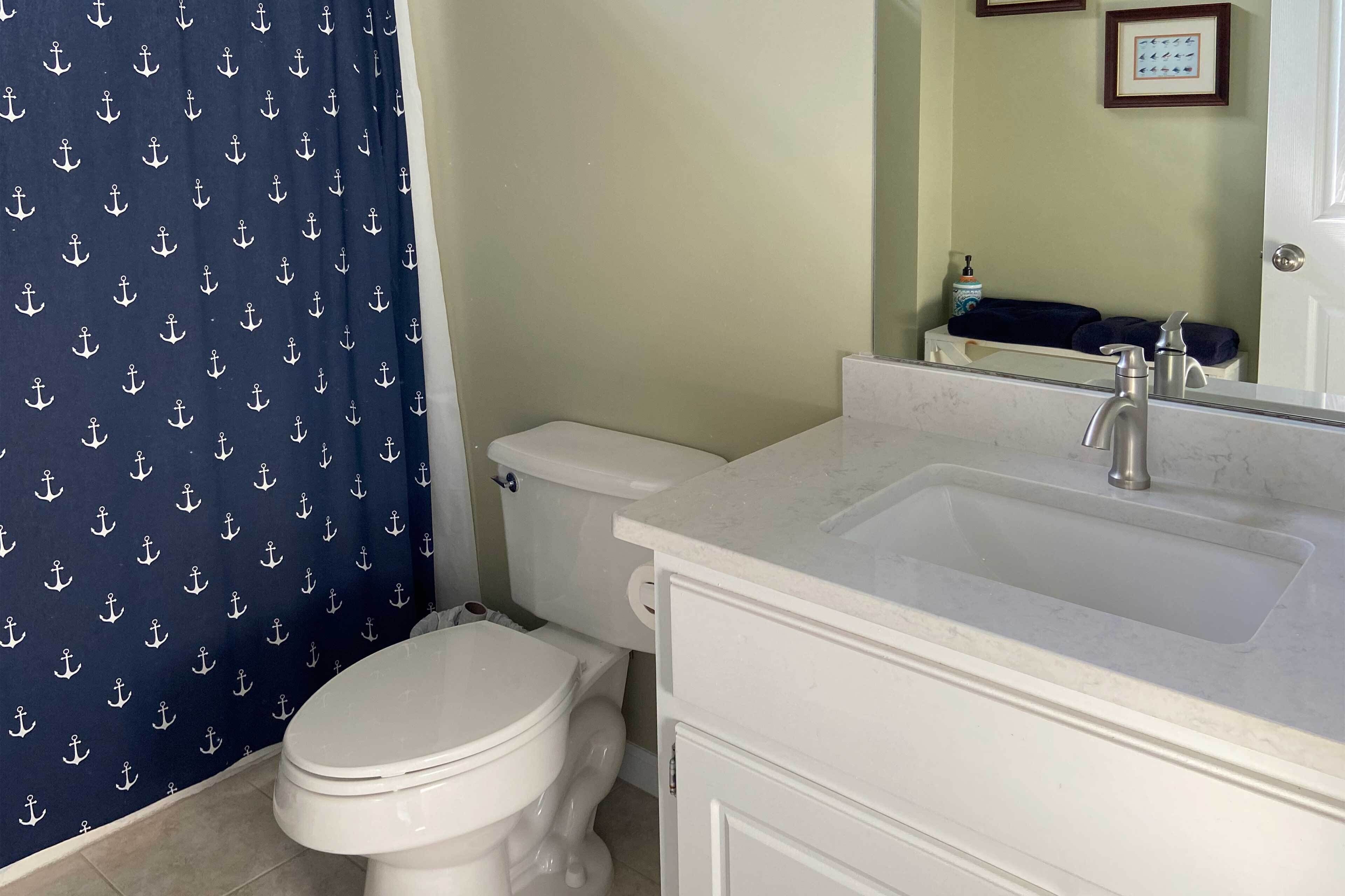 A bathroom with a toilet, a sink, and a shower curtain with anchor patterns.