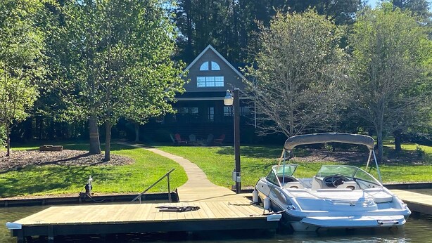 A boat docked at a wooden pier with a house in the background. - Lakefront House With Private Dock + Fire Pit! (Eatonton)