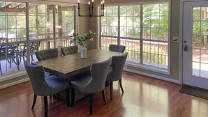A dining area with a wooden table, six grey upholstered chairs, and a chandelier. - Lakefront House With Private Dock + Fire Pit! (Eatonton)