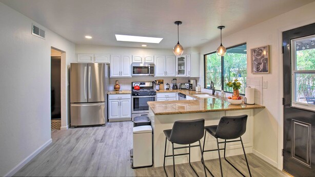 A modern kitchen with stainless steel appliances, white cabinetry, and a central island with bar stools. - Quiet Desert Gem ~ 5 Mi to Saguaro National Park! (Tucson)