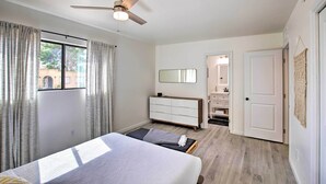 A bedroom with a bed, a ceiling fan, a dresser, a mirror, and a door leading to a bathroom. - Quiet Desert Gem ~ 5 Mi to Saguaro National Park! (Tucson)