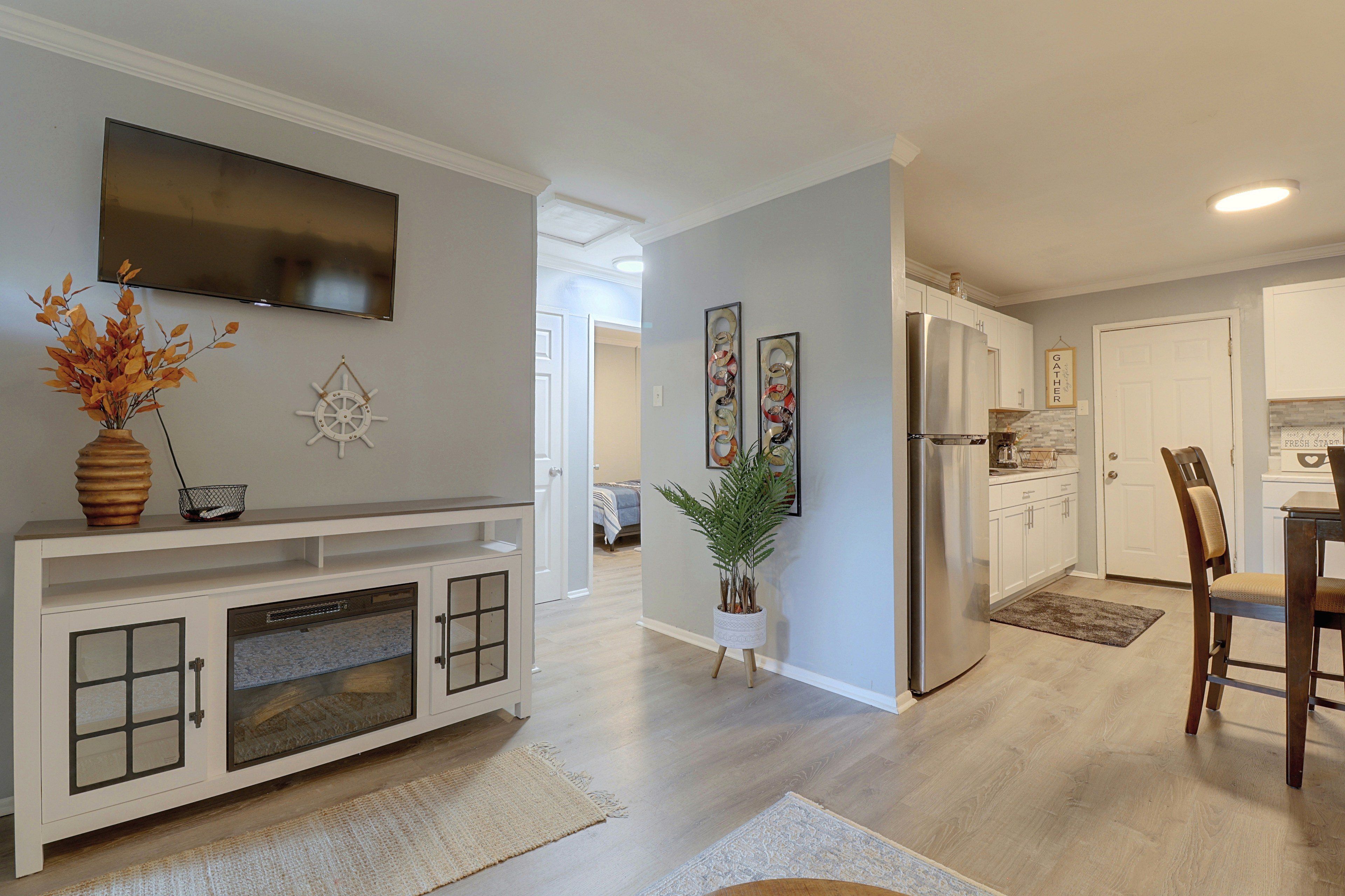 A modern kitchen with a built-in refrigerator, a dining area with a wooden table and chairs, and a living room with a flat-screen TV mounted on the wall.