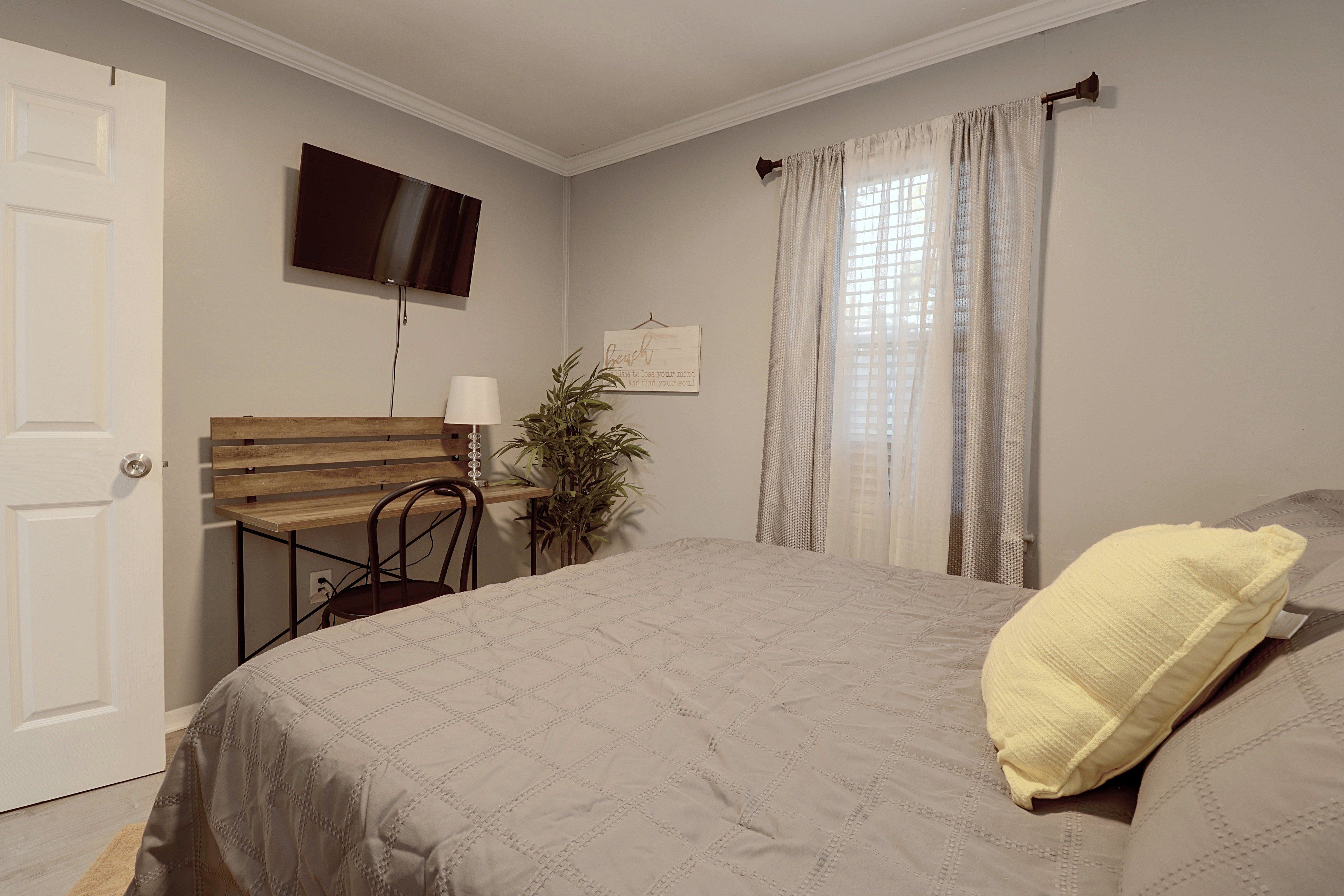 A bedroom with a bed, a desk, a chair, a television, and a window with curtains.