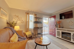 A living room with a sofa, a small table, a television mounted on the wall, and a door leading outside. - Hampton Vacation Rental: Central Location, Patio (Hampton)