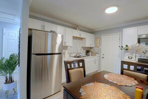 A modern kitchen with white cabinetry, a stainless steel refrigerator, and a dining table with a woven placemat. - Hampton Vacation Rental: Central Location, Patio (Hampton)