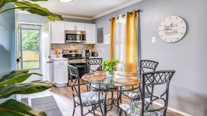 A modern kitchen with white cabinets, a stainless steel microwave, and a dining area with a glass table and metal chairs. - Hampton Vacation Rental: Central Location, Patio (Hampton)