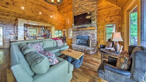 A cozy cabin interior with a stone fireplace, wooden ceiling, and a living area with a sofa and armchairs. - Unique Mineral Bluff Home With Mountain Views! (Mineral Bluff)