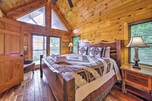 Cozy bedroom with a large bed and patterned quilt, featuring a nightstand and window with blinds.