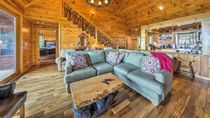 A wooden interior with a sectional sofa, a coffee table, and a staircase leading to a kitchen area. - Unique Mineral Bluff Home With Mountain Views! (Mineral Bluff)