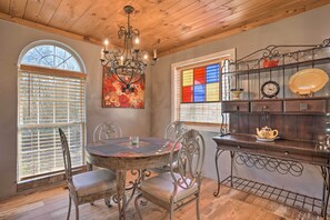 A dining area with a round table, chairs, a chandelier, a stained glass window, and a wall-mounted shelf with decorative items. - Charming Escape w/ Fire Pit in Summerville! (Summerville)