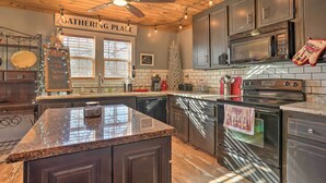 A modern kitchen with dark cabinets, a granite countertop, a stainless steel oven, and a ceiling fan. - Charming Escape w/ Fire Pit in Summerville! (Summerville)