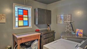 A laundry room with a washing machine, a cabinet, a window with colorful stained glass, and a ceiling fan. - Charming Escape w/ Fire Pit in Summerville! (Summerville)