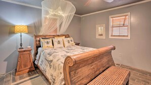 A bedroom with a wooden bed, a ceiling fan, a nightstand with a lamp, and a window with blinds. - Charming Escape w/ Fire Pit in Summerville! (Summerville)