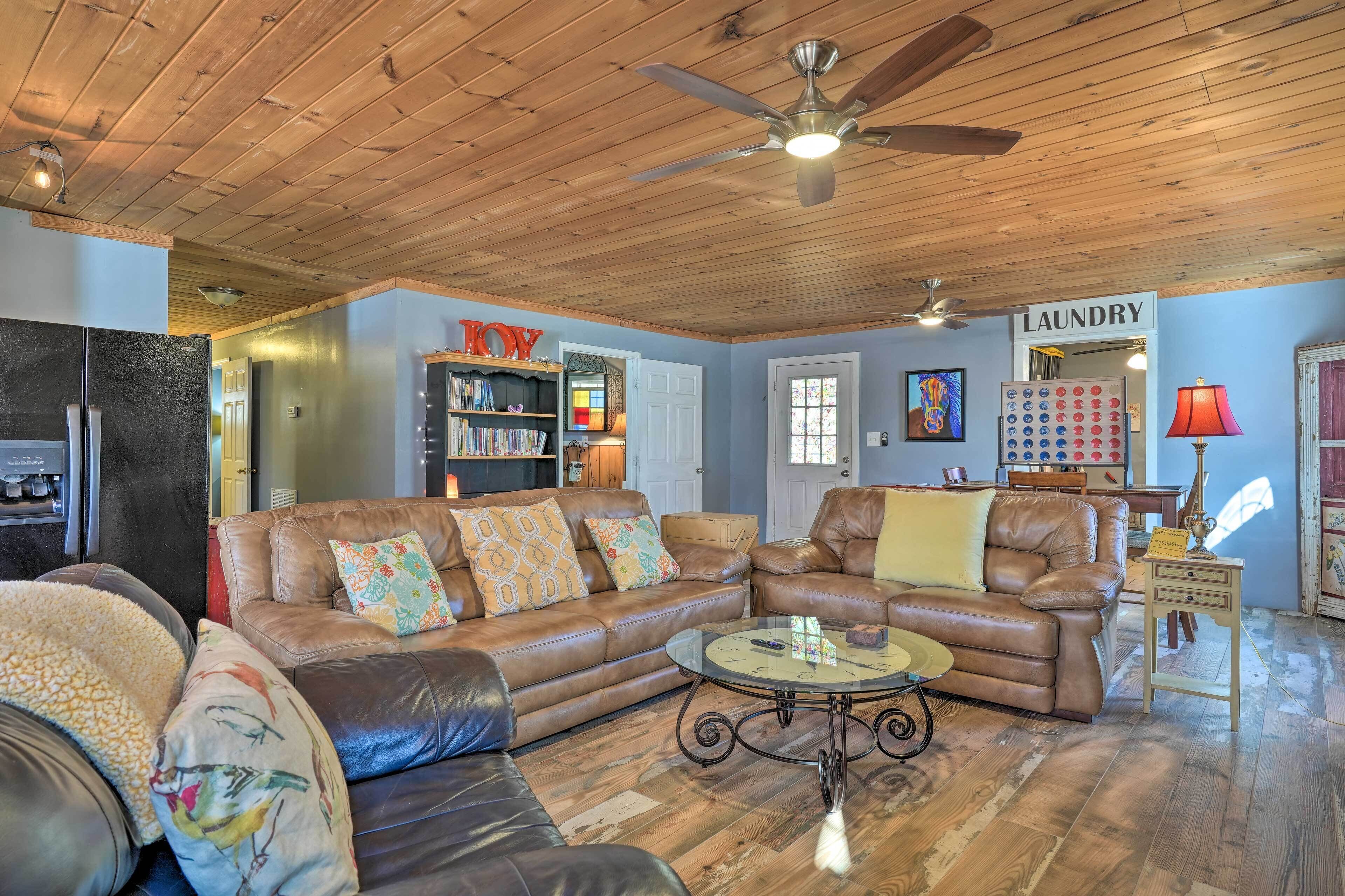 A cozy living room with leather sofas, a coffee table, and a ceiling fan. There is a bookshelf and a sign that says "Laundry."