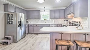 Eine moderne Küche mit grauen Schränken, einem Edelstahl-Kühlschrank, einer weißen Arbeitsplatte und Pendelleuchten.