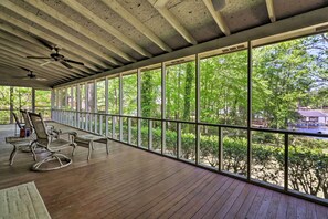 A covered outdoor area with a wooden deck, seating, and large windows offering a view of trees and a building. - Lakefront Milledgeville Cabin: Private Dock, Porch (Milledgeville)
