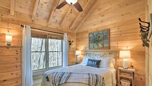 Une chambre à coucher dans un chalet en bois, avec un lit, deux lampes de chevet, une fenêtre avec des rideaux, une commode en bois et un tableau accroché au mur.