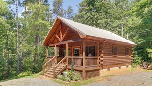 Une cabane en bois dotée d’un porche, d’un escalier et d’une allée en gravier, le tout entouré d’arbres.