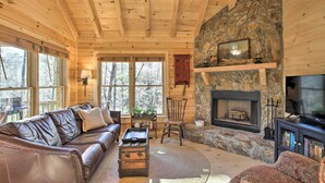 Un intérieur de chalet chaleureux avec une cheminée en pierre, un canapé en cuir et un téléviseur.