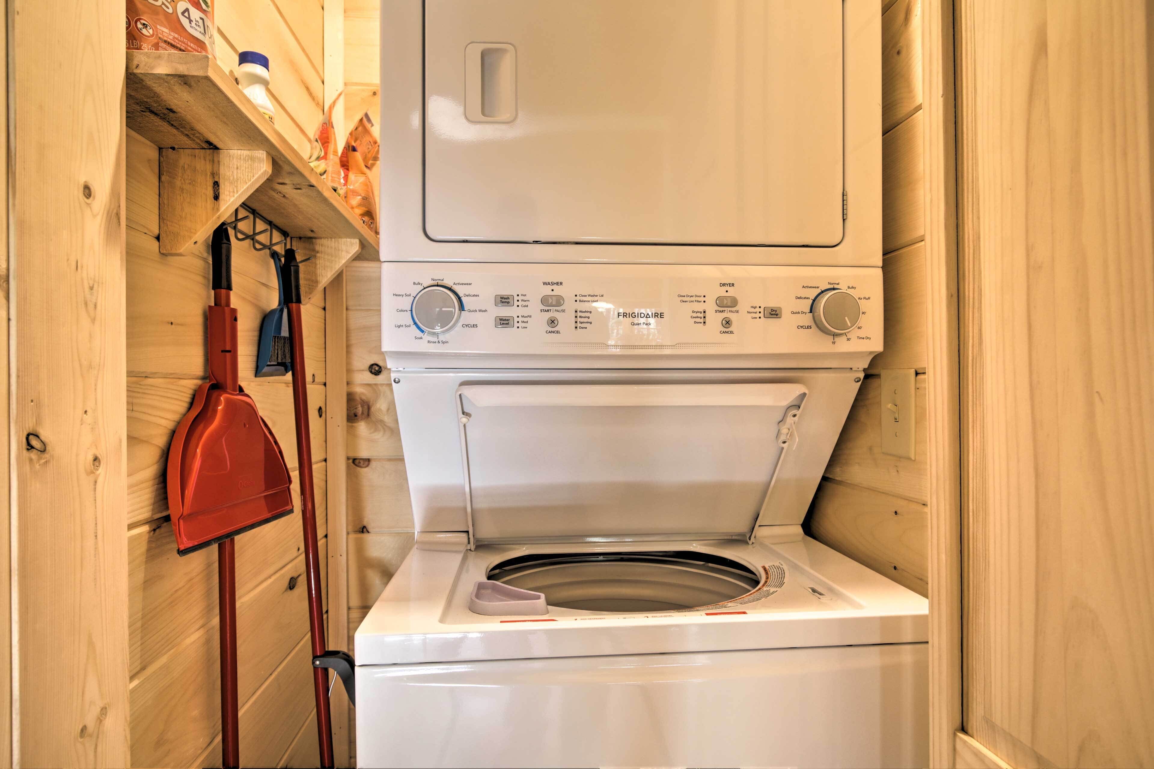 A compact laundry room with a front-loading washing machine, a drying rack, and a red shovel.