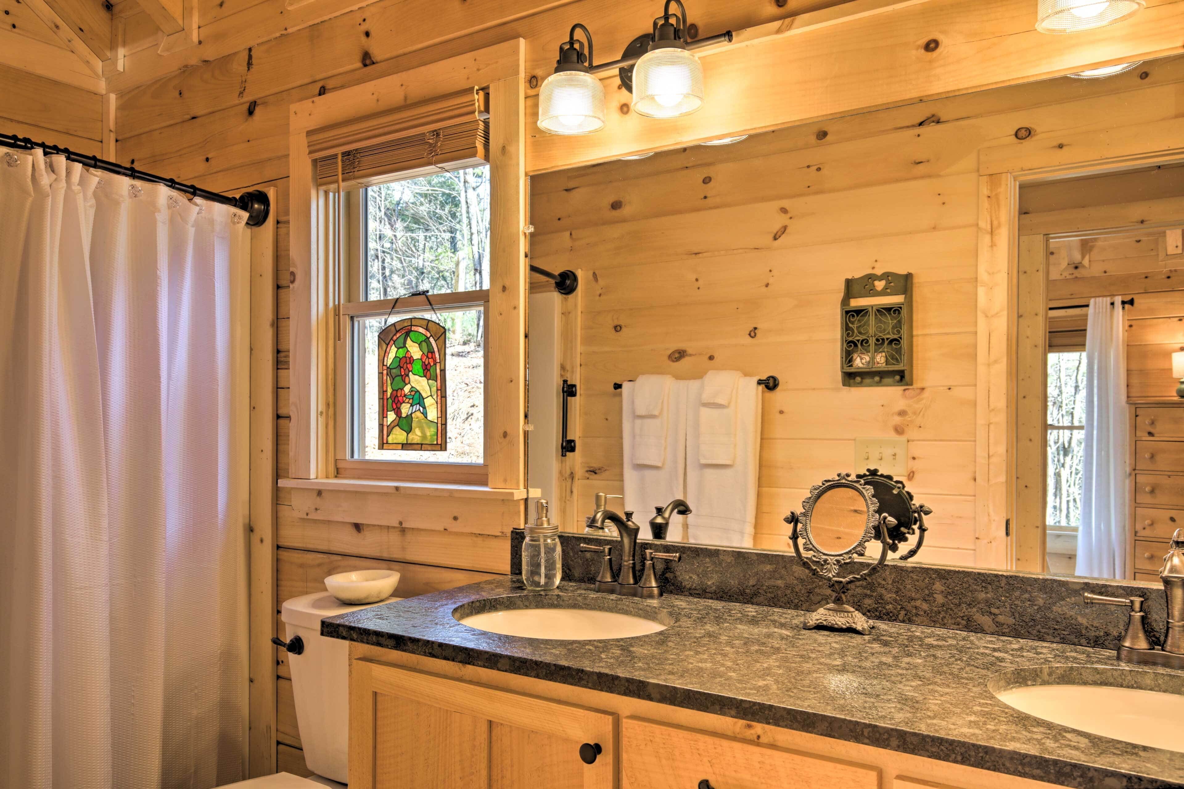Une salle de bain rustique, avec des murs en bois, un grand miroir, deux lavabos et une fenêtre à vitraux.