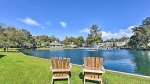 Duas cadeiras Adirondack de frente para um lago, com um coreto e uma fonte ao fundo.