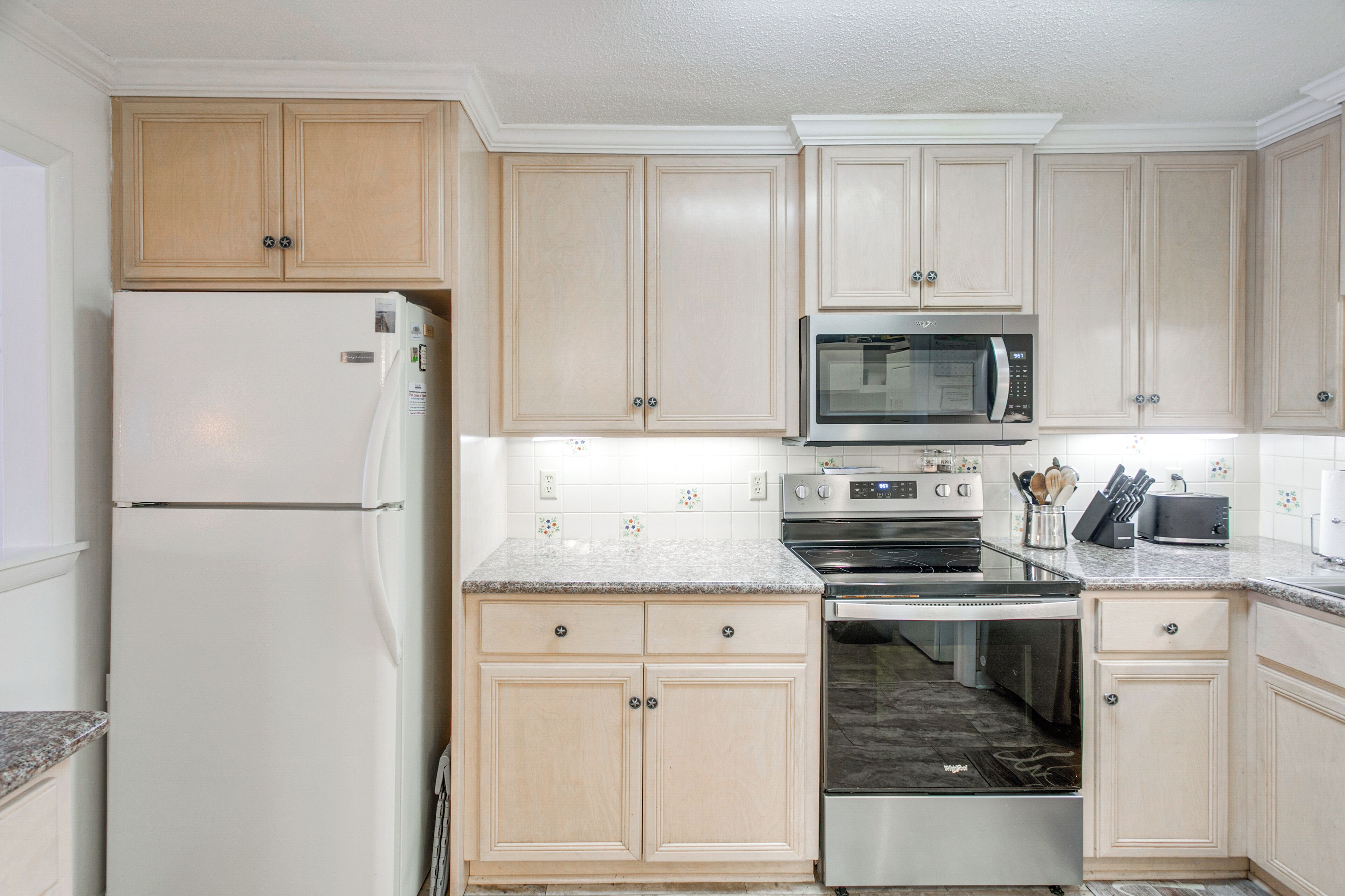 A kitchen with light wooden cabinets, a stainless steel refrigerator, a microwave, an oven, and a dishwasher.