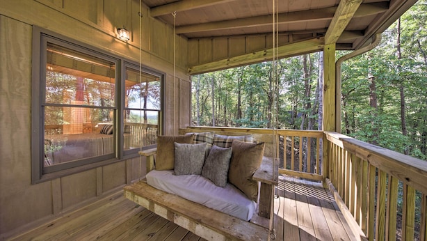 A wooden deck with a cushioned seating area, large windows, and a view of the surrounding forest. - Blue Ridge Hideaway w/ Fire Pit & Mtn Views! (Blue Ridge)