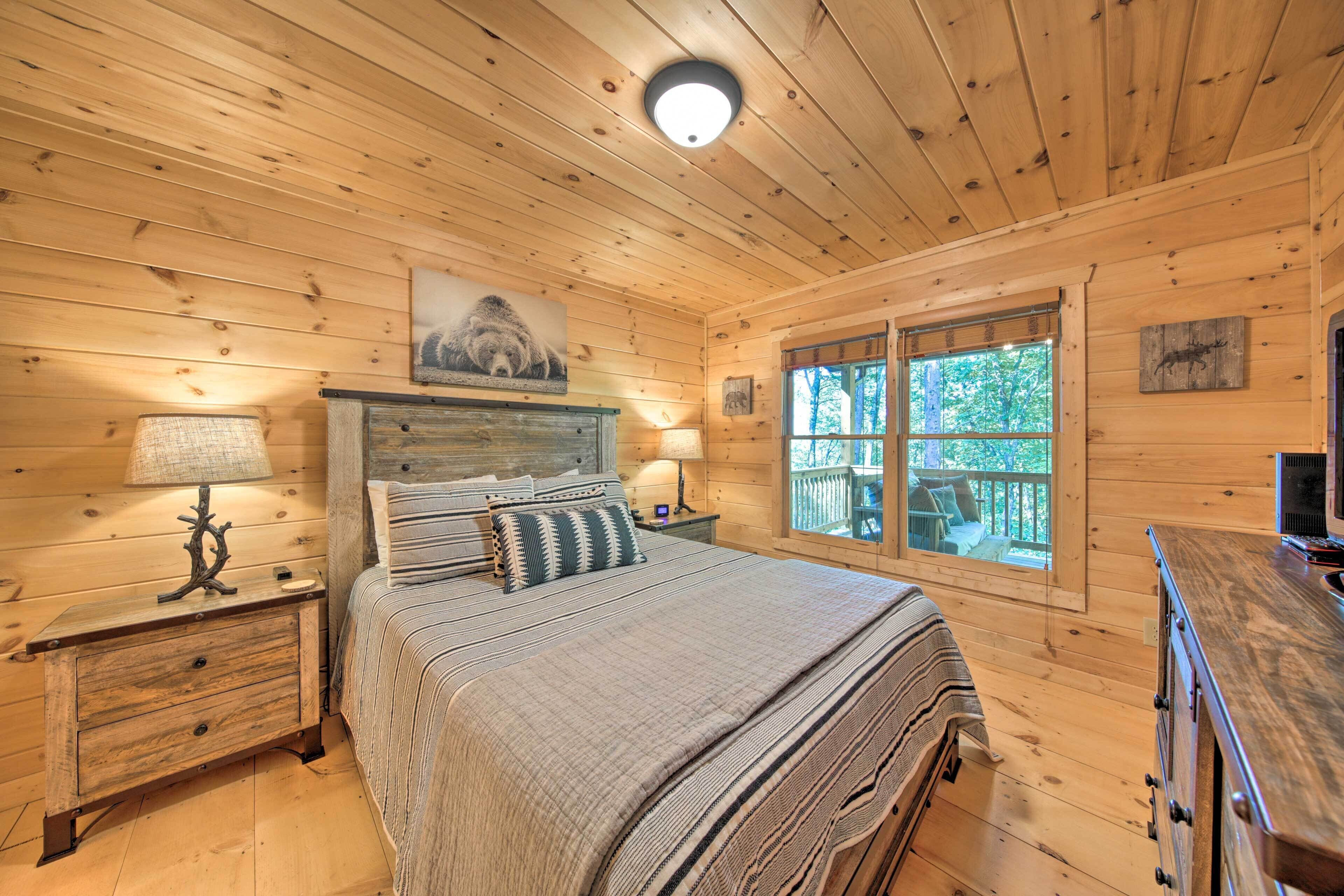 A wooden cabin bedroom with a bed, nightstands, a dresser, and a window with a view of trees.