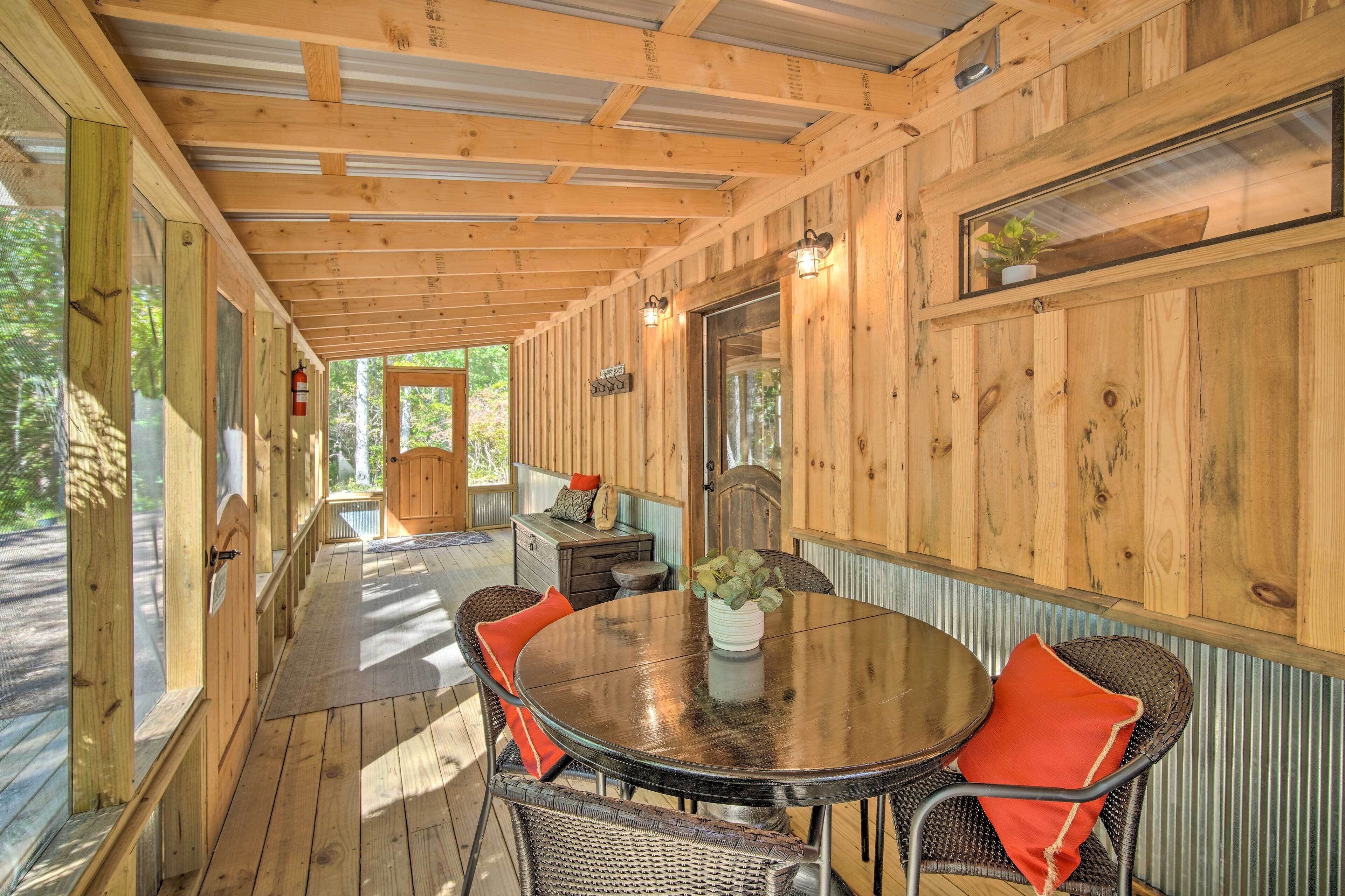 A wooden deck with a round table and chairs, a small table with a plant, and a door leading to another room.