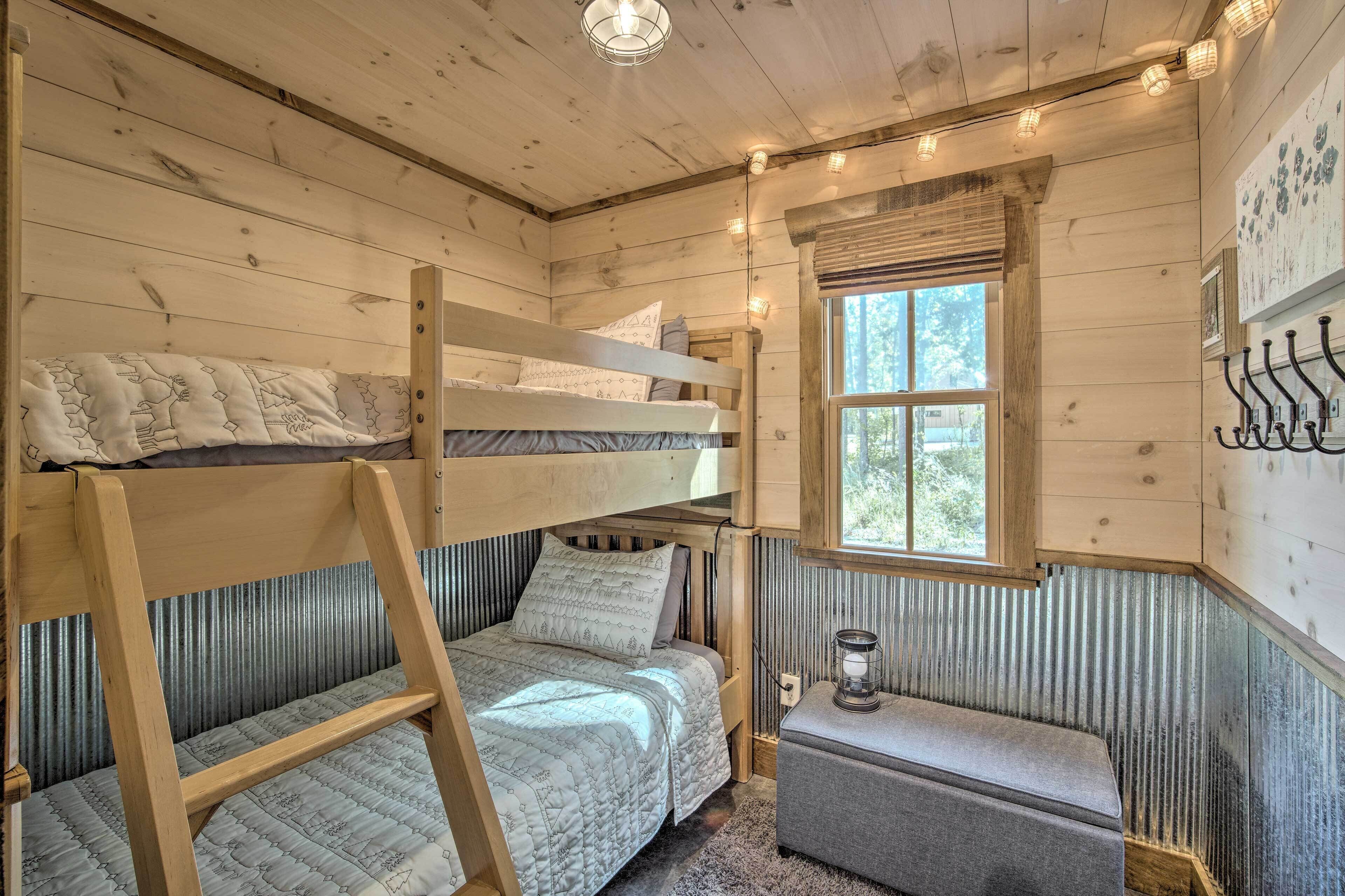 A cabin with a bunk bed, a small bench, a window, and a wall-mounted light fixture.