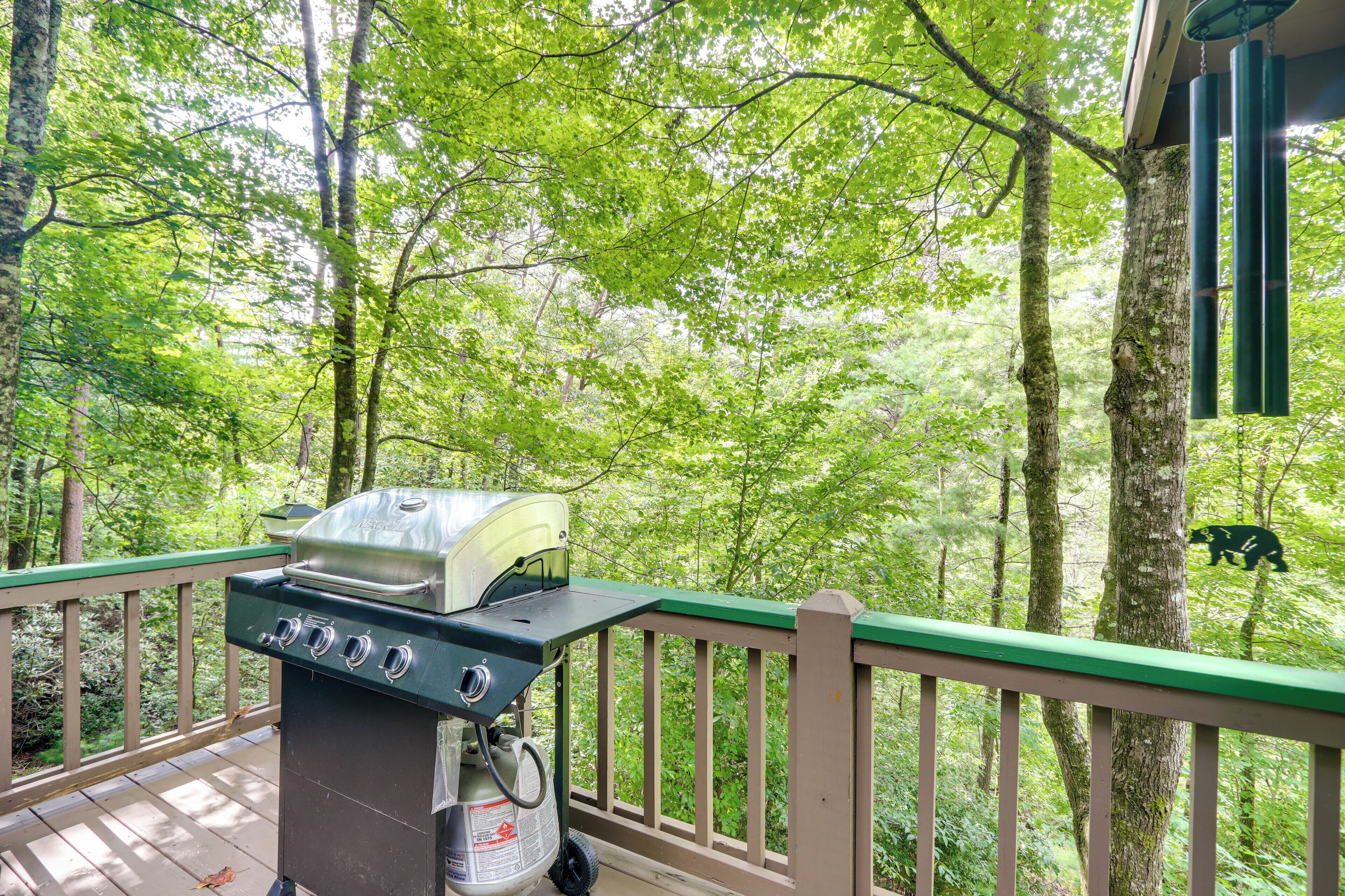 A barbecue grill on a wooden deck with a view of a forest.