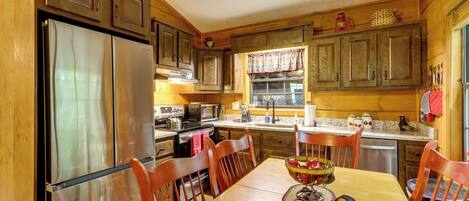 A kitchen with wooden cabinets, a stainless steel refrigerator, a dining table with chairs, and a window with curtains.