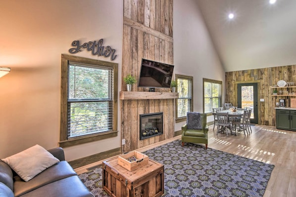 A spacious living room with a fireplace, a television mounted on the wall, and a dining area with a table and chairs.