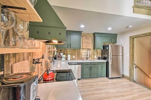 A kitchen with wooden cabinets, a stainless steel refrigerator, a red kettle, and a built-in oven.